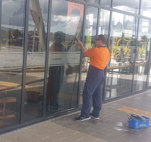 Commercial window cleaner using squeegee for streak-free glass at an Indian Cuisine kingfisher restaurant chch nz